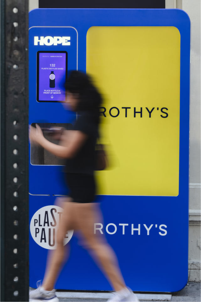 Person walking past a large blue and yellow advertisement for Rothy's shoes.