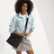 hover | The Mini Zip Bucket in Black Sand worn as a crossbody by a female model, shown in motion from the right.