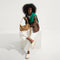 Alternate view of The Daily Crossbody in Hazelnut, carried by its top handle by a female model, shown from the front.