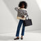 Alternate view of the Classic Tote in Black Sand, carried by its top handles by a model, shown from front.
