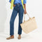 An alternate view of a model holding The Zip Travel Tote in Parchment Basketweave.