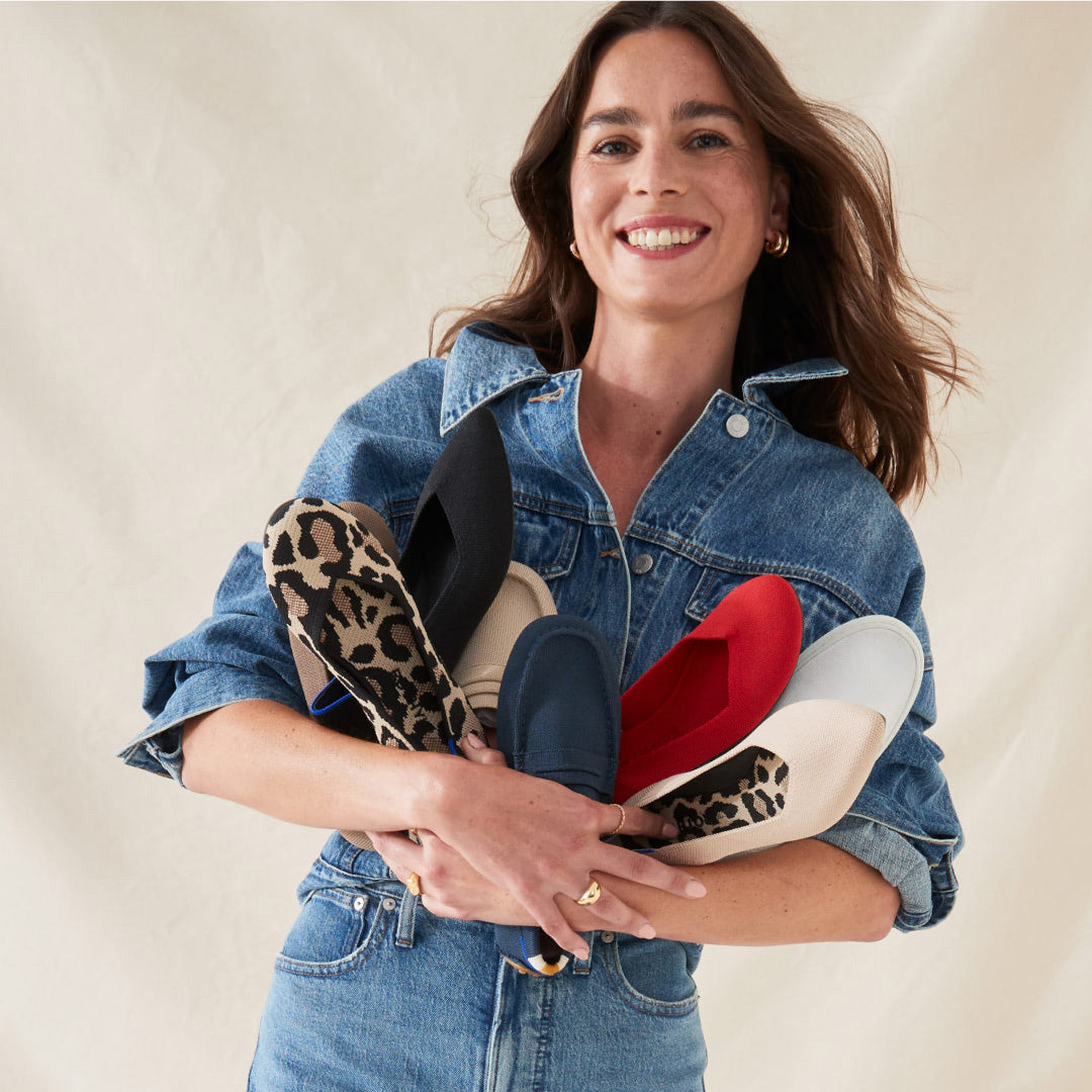 A model carrying a variety of Rothy's shoes in her hands.