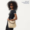 The Mini Zip Bucket in White Sand worn as a crossbody by a female model, shown in motion from the right.