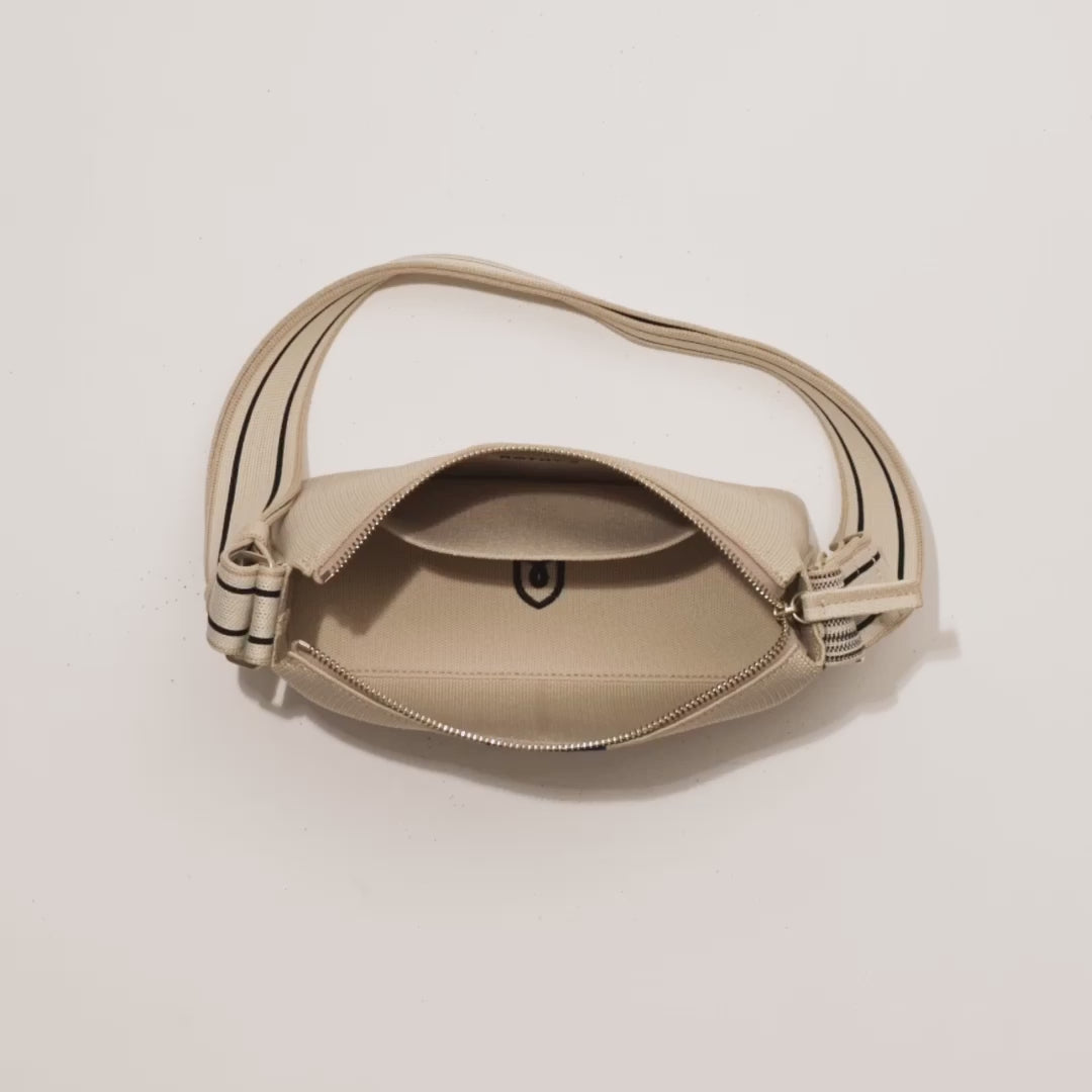 The Casual Crossbody in Parchment shown packed with an iPhone, The Slim Card Case in Grey Houndstooth, makeup, glasses, a notebook, AirPods and lipgloss. A female model then zips up the bag and carries it out of frame.