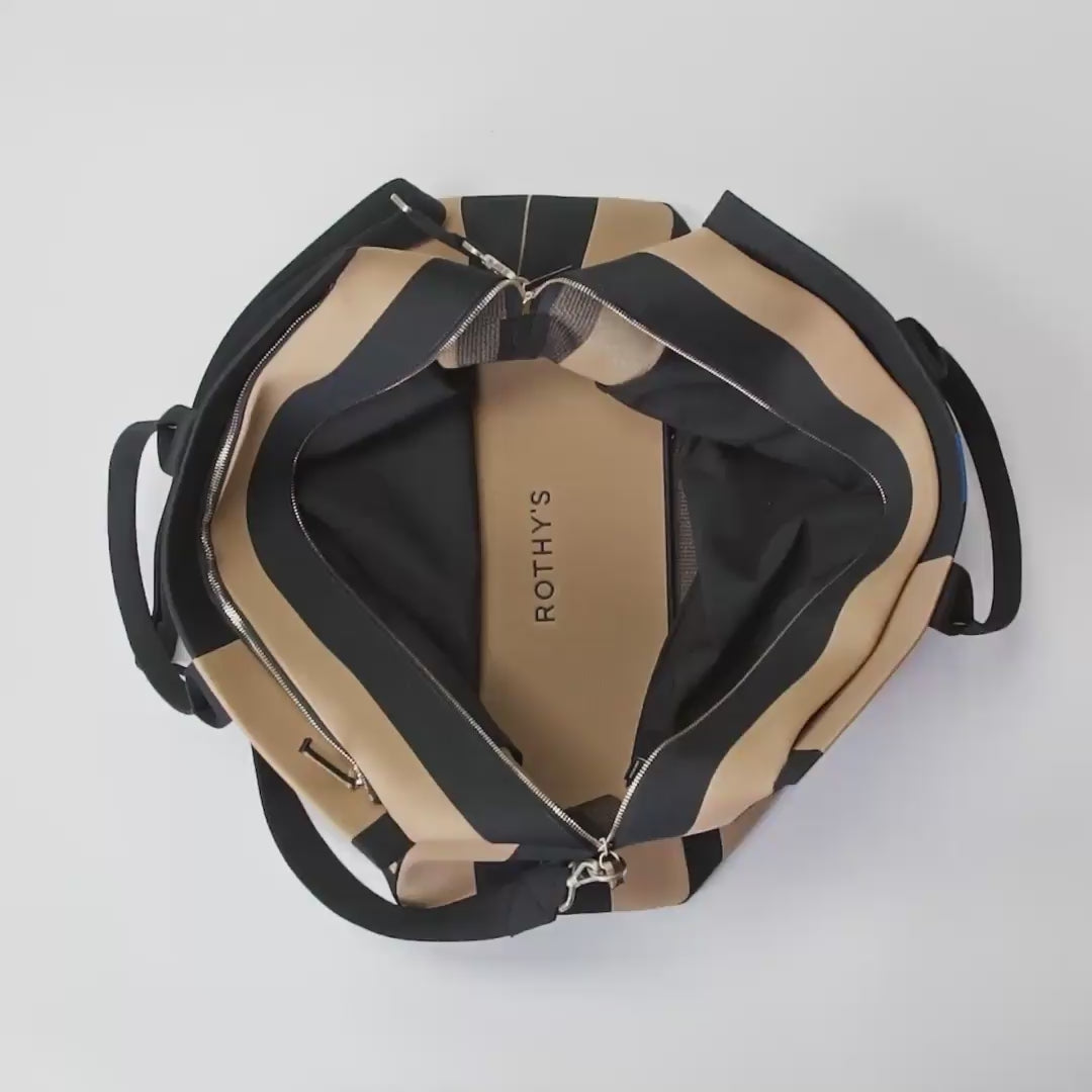 The main compartment of the Weekender in Camel and Black shown being packed with clothes, the City Slip On, the Loafer, a pouch and a throw blanket. One side pocket of the Weekender is then packed with a laptop. The other side pocket is packed with a mini pouch, and the interior zip pocket is packed with an iPhone. The Weekender is then picked up by the handles and pulled out of frame. 