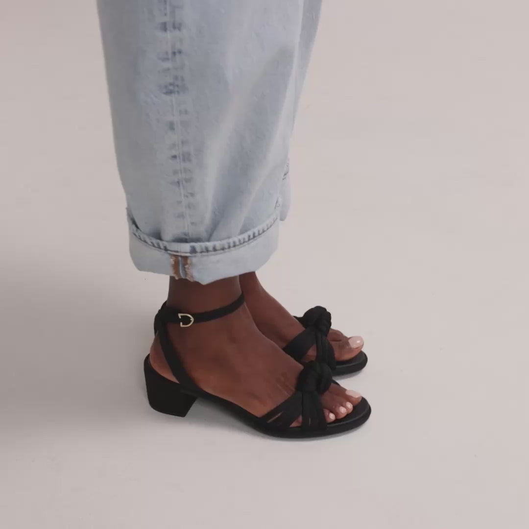 Model walking in The Knot Sandal in Black and showing different angles of the shoes. 